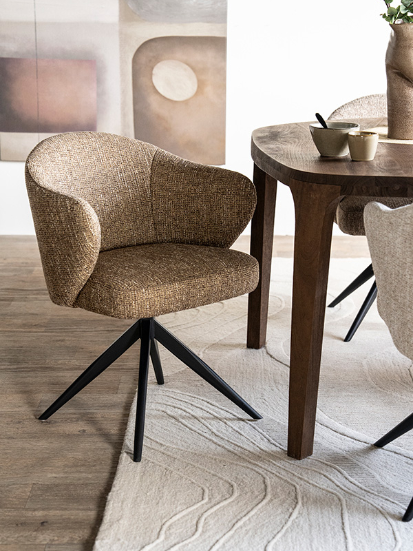 Draaibare eetkamerstoel met bruine gemêleerde bekleding en zwart metalen onderstel aan een houten eettafel op een licht vloerkleed.